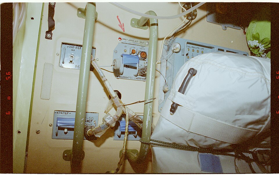 Interior view of the Mir space station’s docking node, showing hatches and cables trailing through a cramped, worn module.